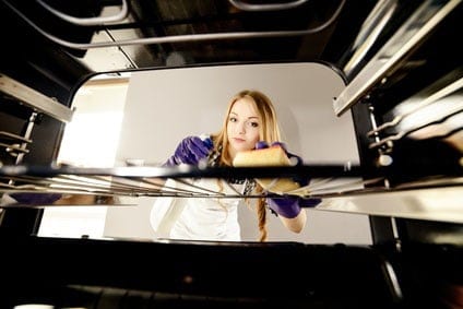femme nettoie l’intérieur de son four avec une éponge