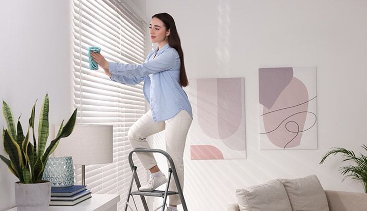 Femme sur un escabeau nettoyant un store