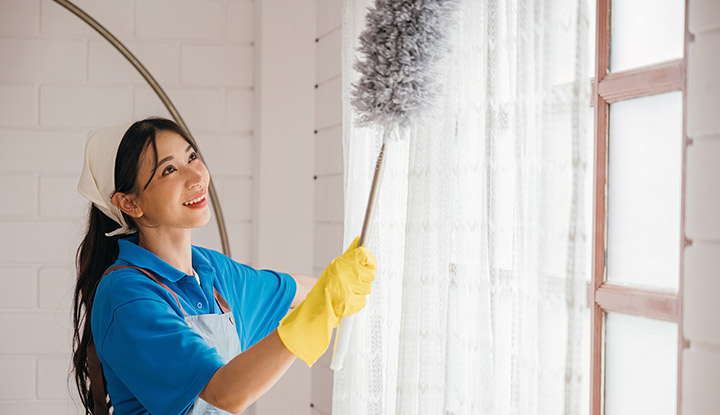 Une femme qui nettoie des rideaux avec un plumeau