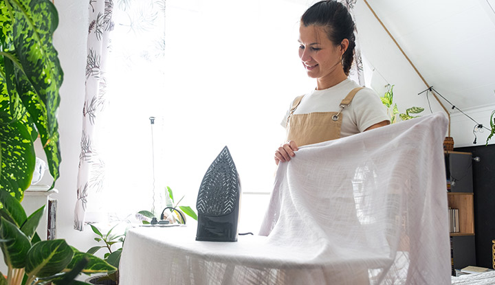 Une femme qui repasse des rideaux avec un fer à repasser